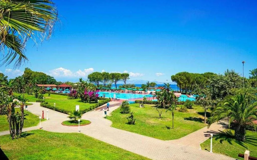 Vista panoramica del giardino del resort con piscina, ombrelloni e mare sullo sfondo