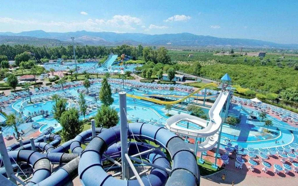 Parco acquatico visto dall'alto con scivoli, piscine a onde e fiume lento circondato da montagne