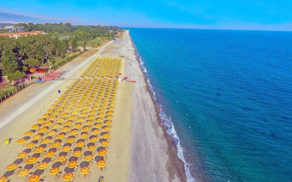 Veduta aerea della lunga spiaggia con ombrelloni gialli ordinati e mare azzurro cristallino