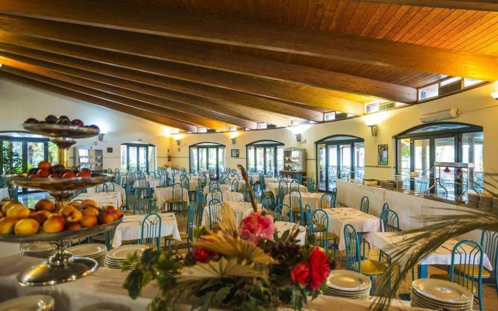 Sala ristorante interna con soffitto in legno, tavoli apparecchiati e buffet di frutta in primo piano