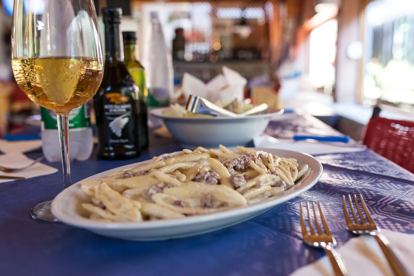 Piatto di pasta fresca con ragù bianco accompagnato da un calice di vino