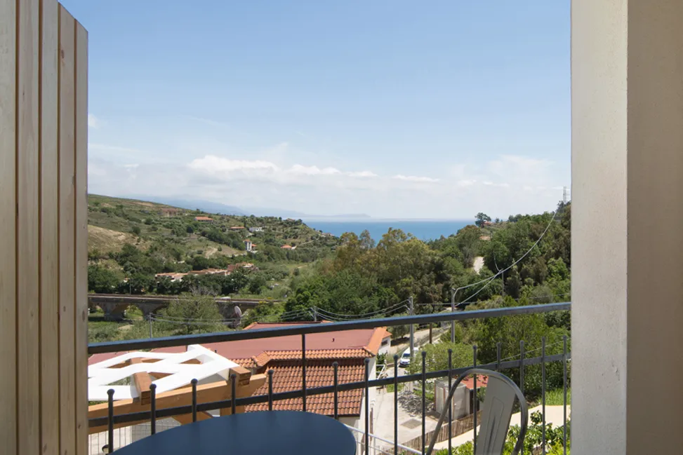 Balcone con tavolino e sedie affacciato su colline verdi e mare all'orizzonte