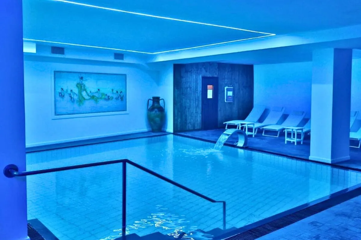 Piscina interna illuminata di blu con lettini relax e cascata d'acqua
