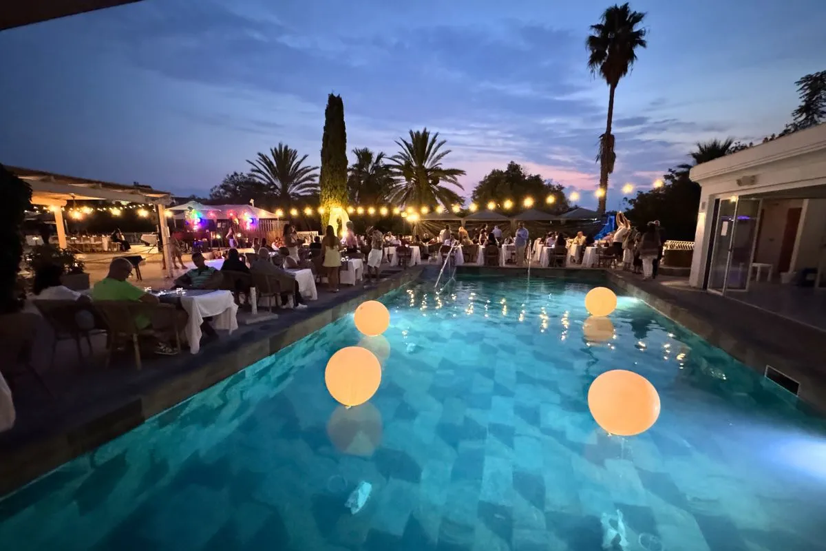 Cena serale a bordo piscina con luci decorative e palloncini luminosi in acqua