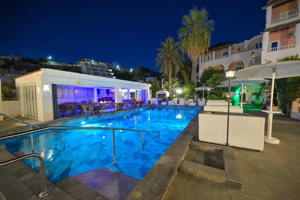 Piscina illuminata di sera con area ristorante e lounge sullo sfondo