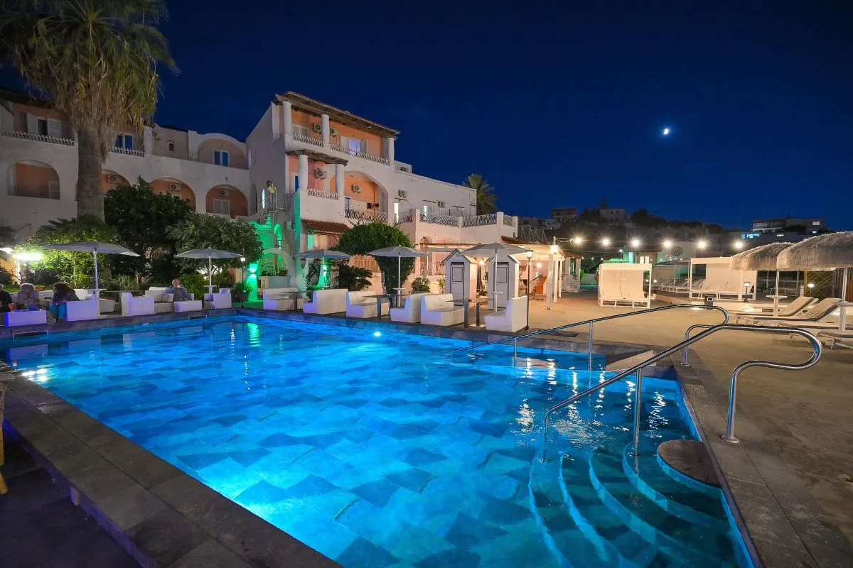 Piscina esterna illuminata di notte con edificio dell'hotel e luna