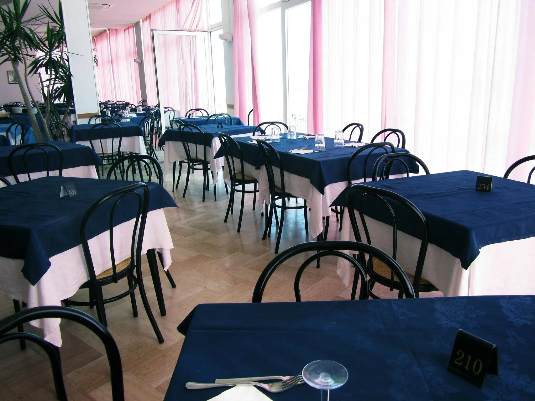Sala ristorante con tovaglie blu, sedie nere e tende rosa
