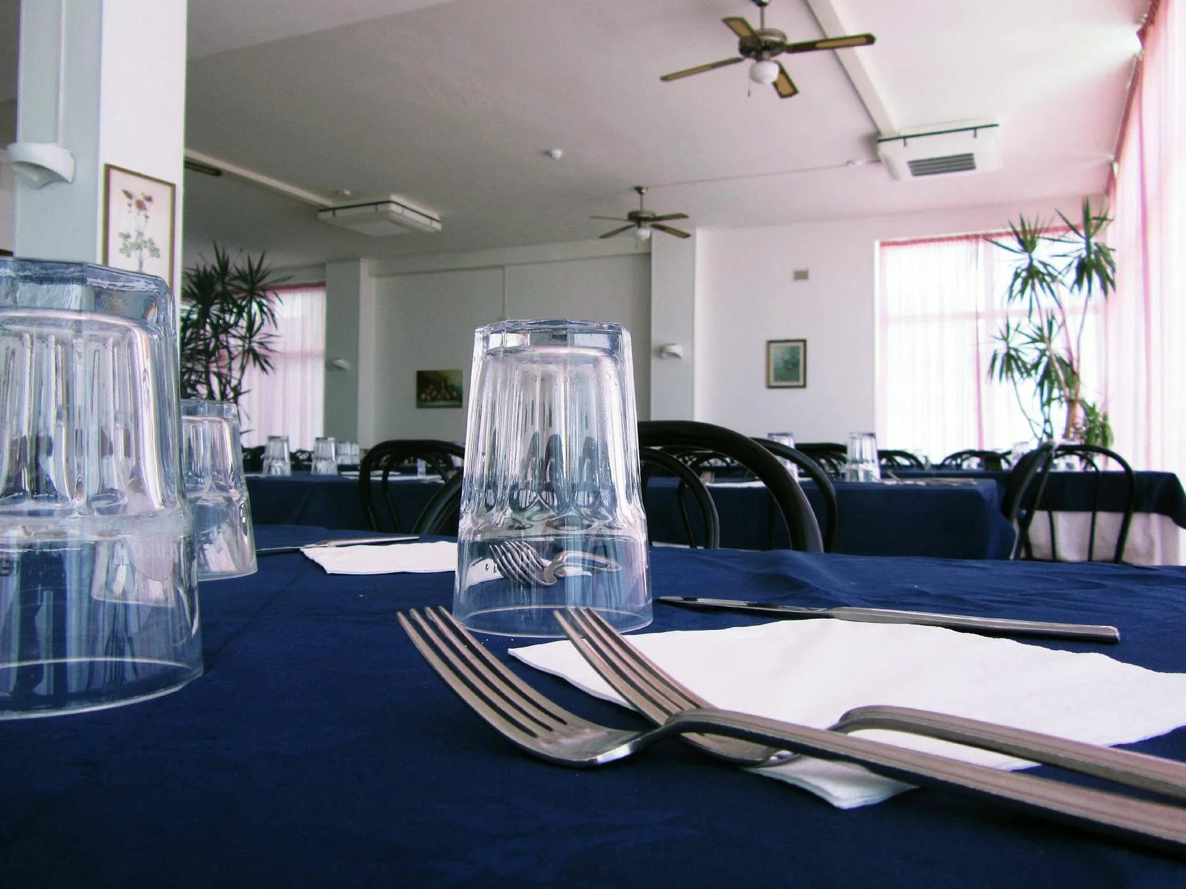 Sala da pranzo con tavoli blu apparecchiati con bicchieri e posate