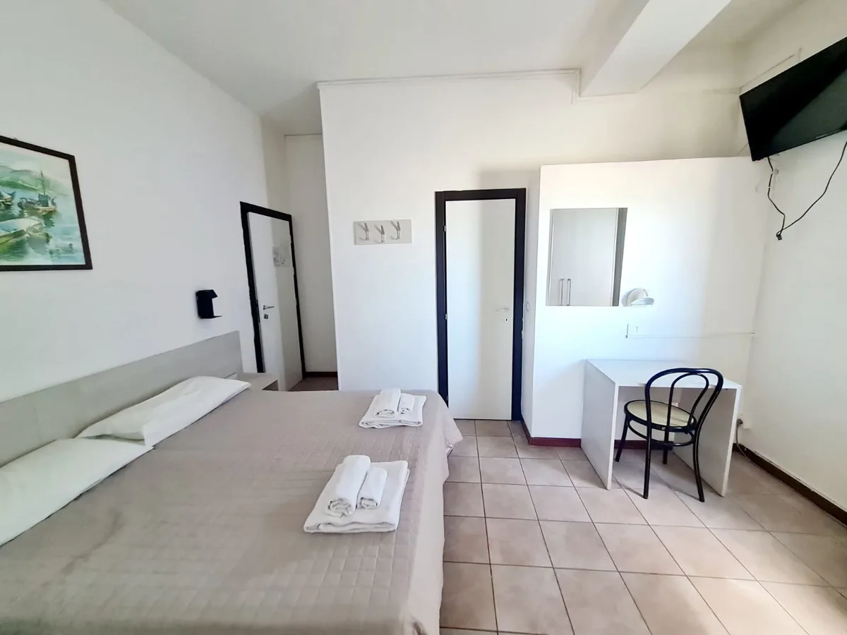 Camera matrimoniale luminosa con scrivania, TV e asciugamani sul letto