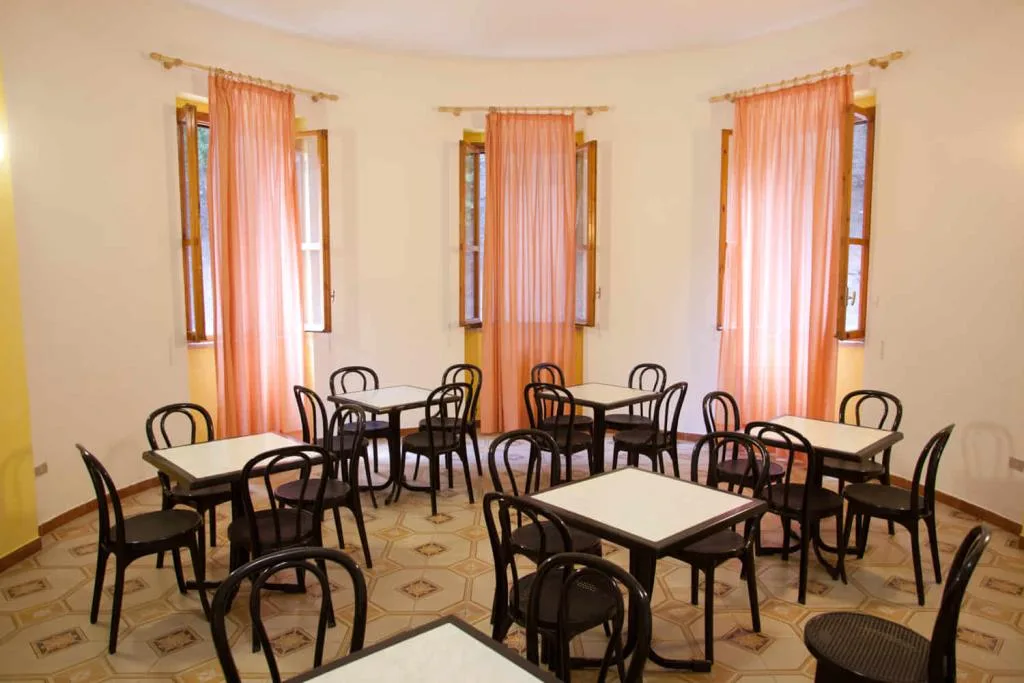 Sala colazione con tavolini bianchi, sedie nere e tende arancioni