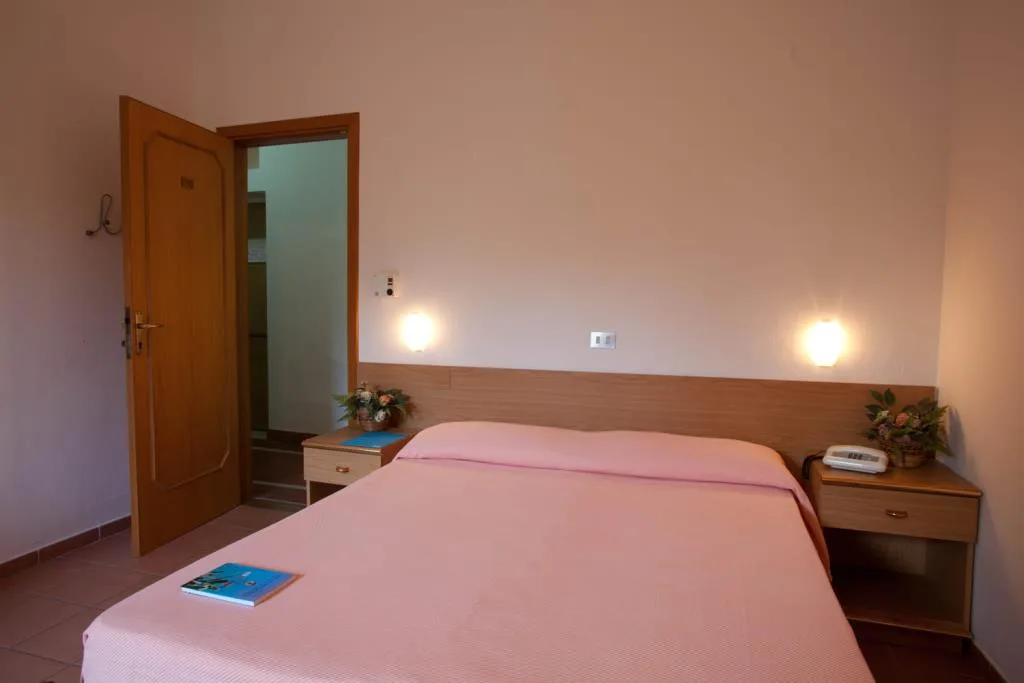 Camera con letto matrimoniale, copriletto rosa e comodini in legno