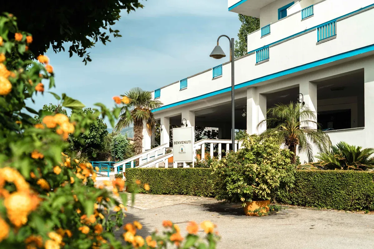 Ingresso dell'hotel con insegna di benvenuto, palme e fiori arancioni