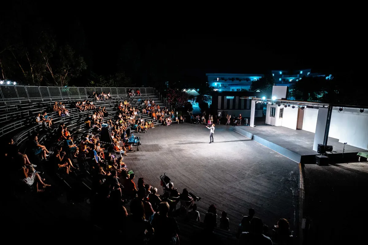 Anfiteatro illuminato di sera con spettacolo e pubblico sulle gradinate