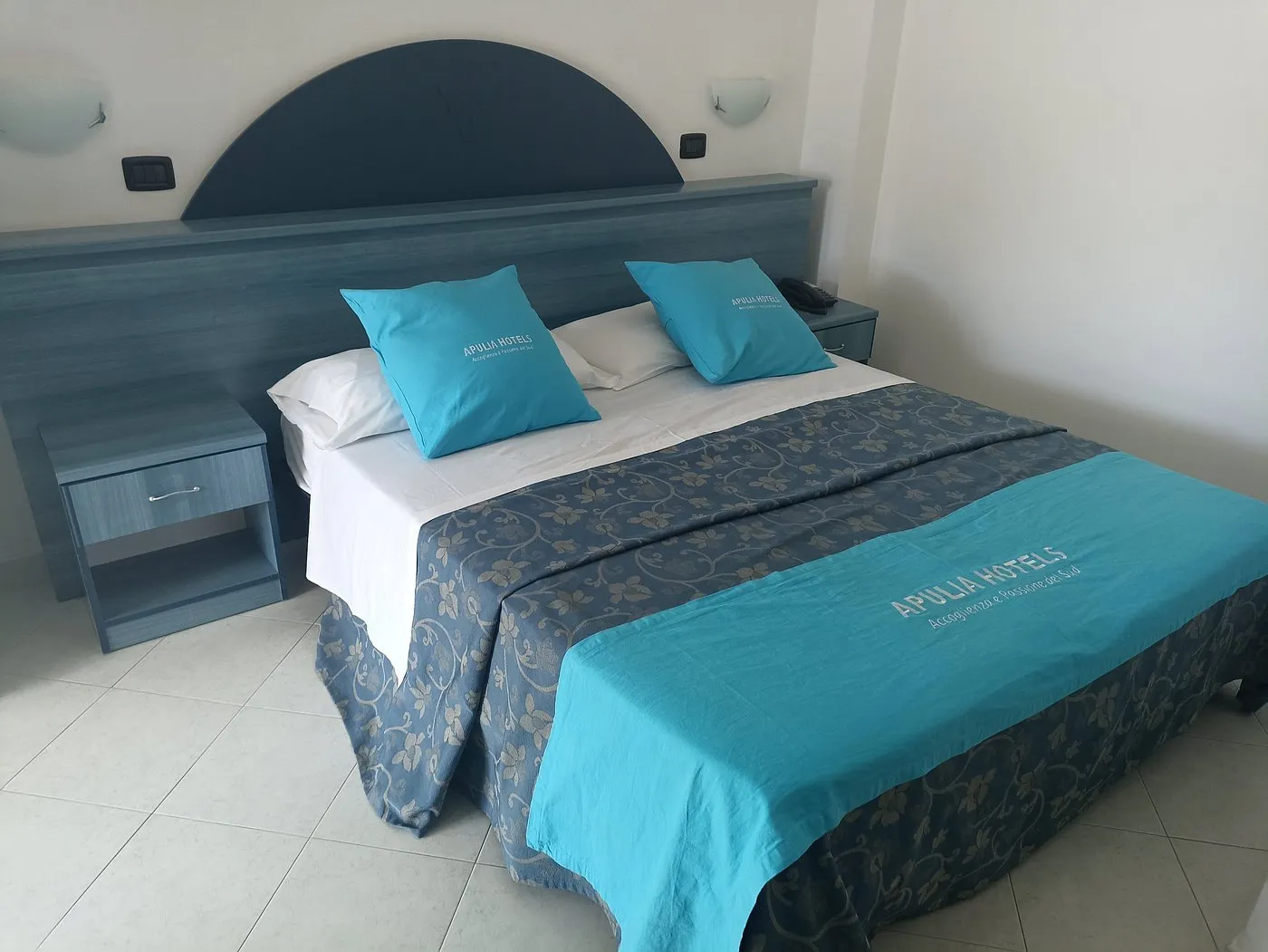 Letto matrimoniale con cuscini Apulia Hotels e comodino azzurro