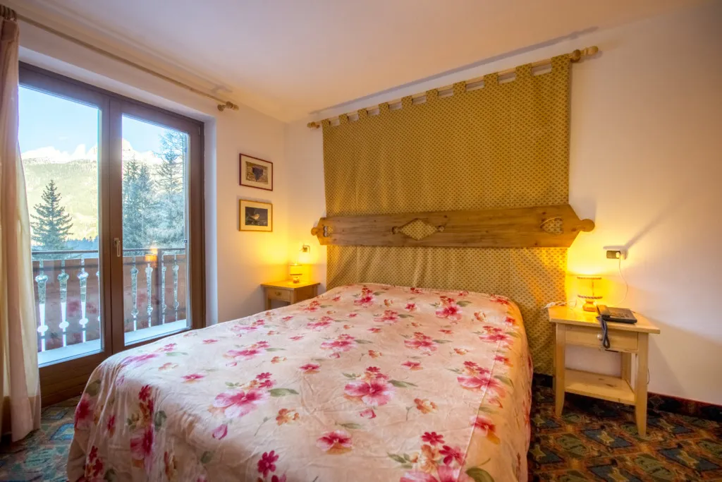 Camera da letto con letto matrimoniale, testiera in legno e finestra con vista sulle montagne