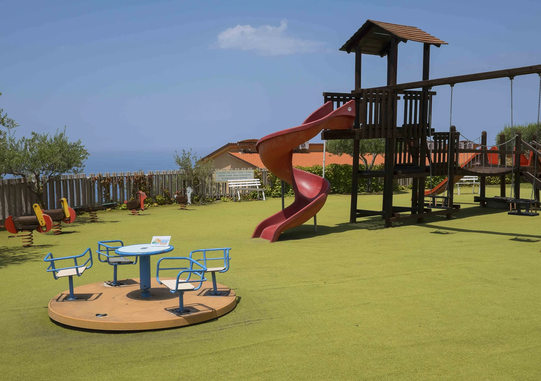 Area giochi con scivolo a spirale, giostrina e vista sul mare