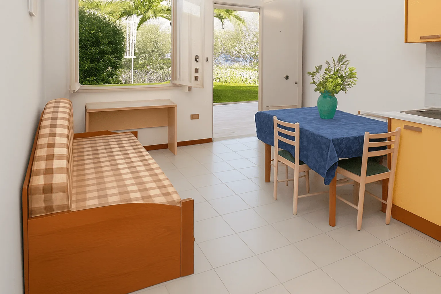 Interno di appartamento con angolo cottura, divano letto e tavolo con vista giardino