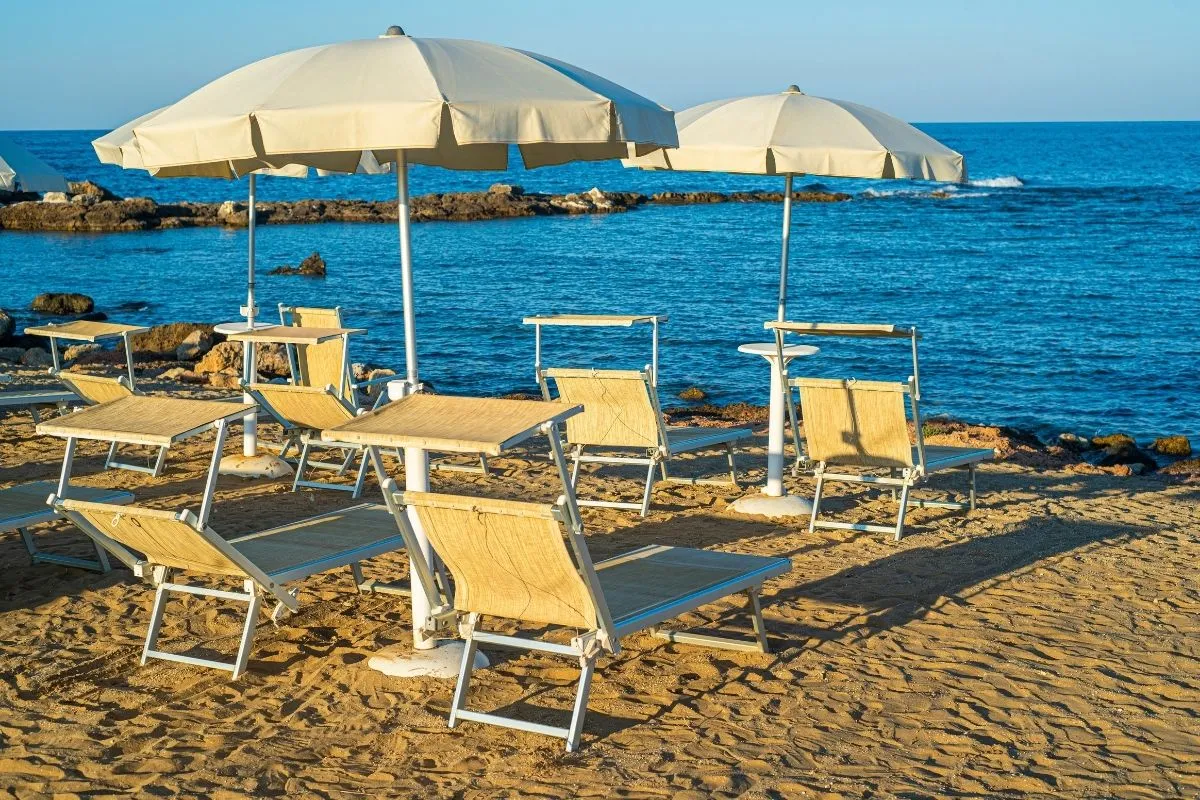 Lettini e ombrelloni bianchi sulla spiaggia con mare blu e scogli