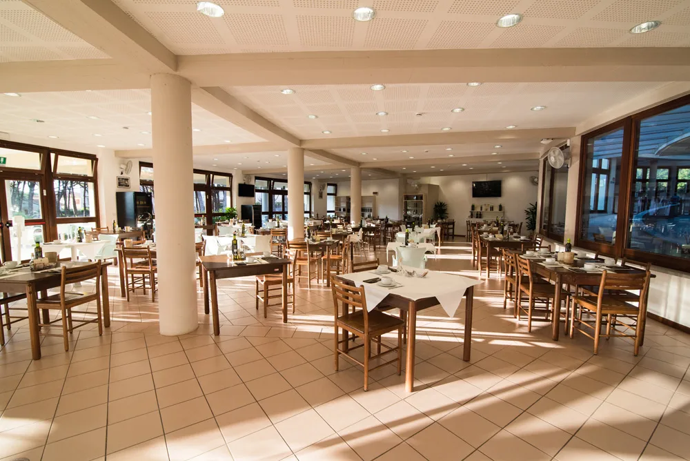 Ampia sala ristorante luminosa con tavoli in legno e sedie impagliate apparecchiati