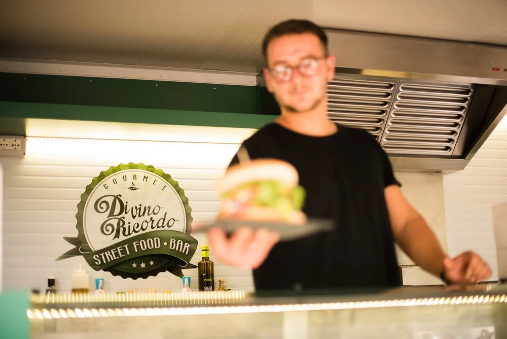 Addetto dello street food bar che serve un panino gourmet al bancone
