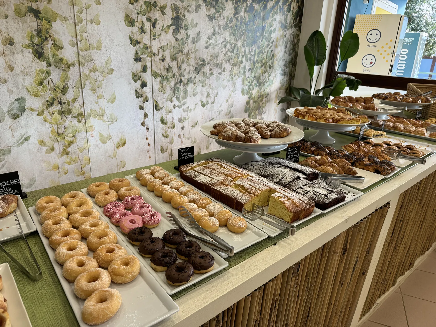 Buffet della colazione con ciambelle, cornetti e torte assortite su banco di bambù