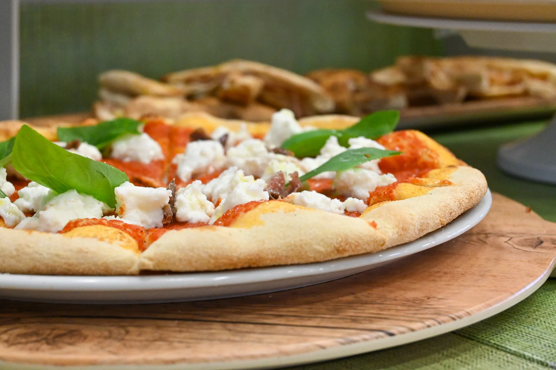 Pizza con pomodoro, ricotta e basilico servita su tagliere di legno