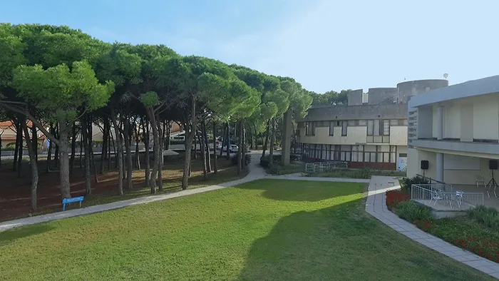 Giardino verde con prato curato, pini marittimi ed edifici del complesso