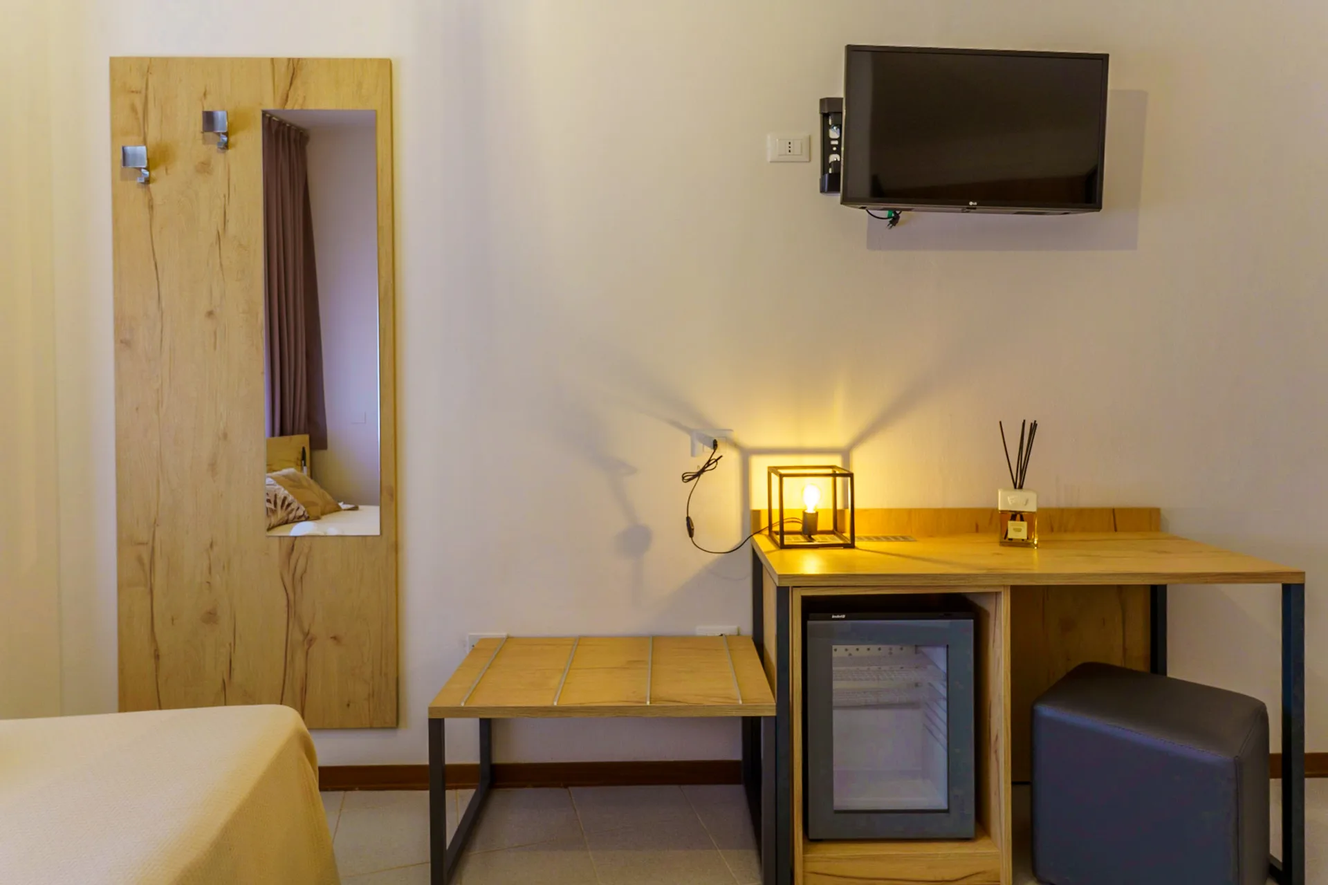 Angolo camera con scrivania in legno, minibar, TV a parete e lampada d'atmosfera