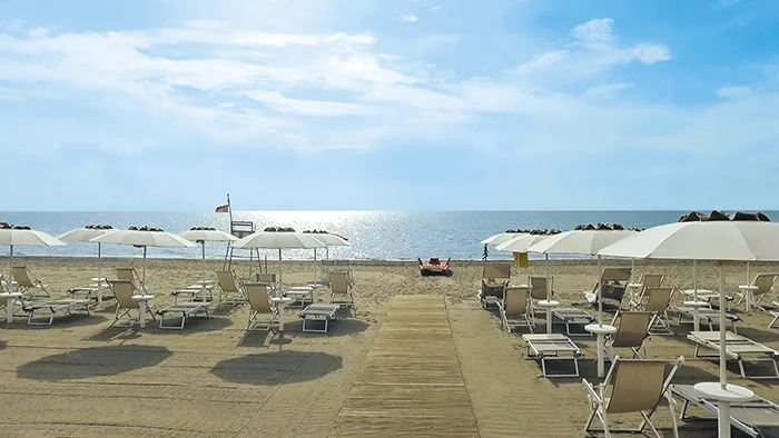 Spiaggia attrezzata con lettini e ombrelloni bianchi e passerella verso il mare luminoso