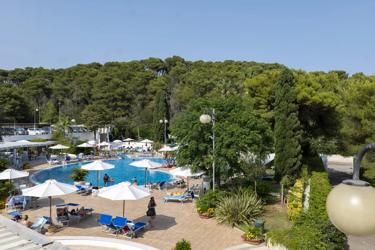 Area piscina vista dall'alto con lettini blu, ombrelloni bianchi e rigogliosa vegetazione sullo sfondo