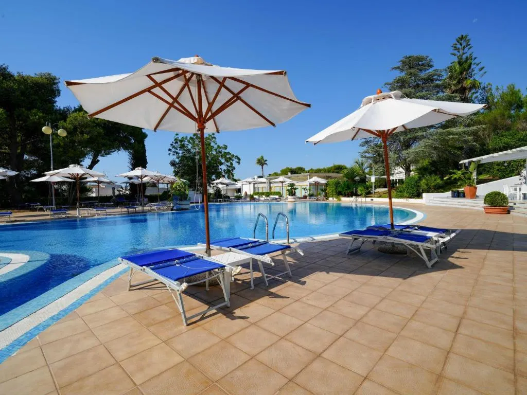 Lettini blu e ombrelloni bianchi in legno sul bordo piastrellato di una piscina azzurra