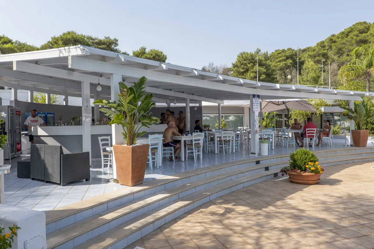 Bar esterno con pergolato bianco, tavoli e sedie, immerso nel verde