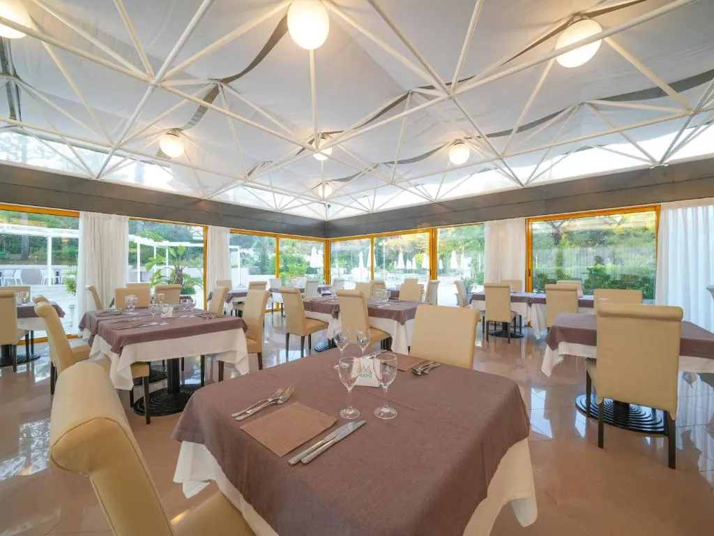Sala ristorante luminosa con soffitto in tela, tavoli apparecchiati e ampie vetrate sul verde