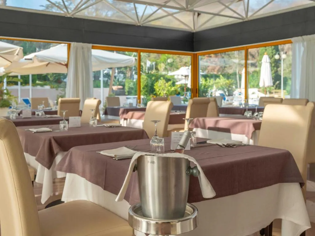Sala ristorante con tavoli apparecchiati, tovaglie color prugna e cestello per il vino, con vista sul giardino
