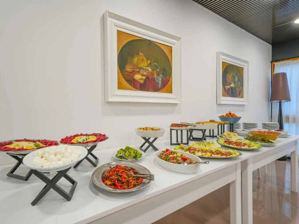 Buffet di antipasti con affettati, mozzarelle, insalate e verdure sotto quadri di nature morte