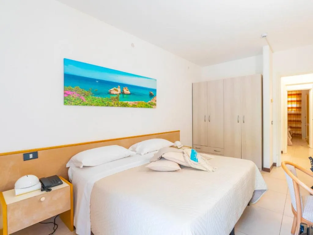 Camera matrimoniale luminosa con letto bianco, armadio in legno chiaro e quadro del mare