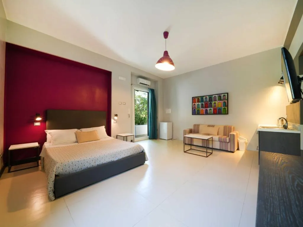 Camera moderna con parete bordeaux, letto matrimoniale, divano e angolo cottura
