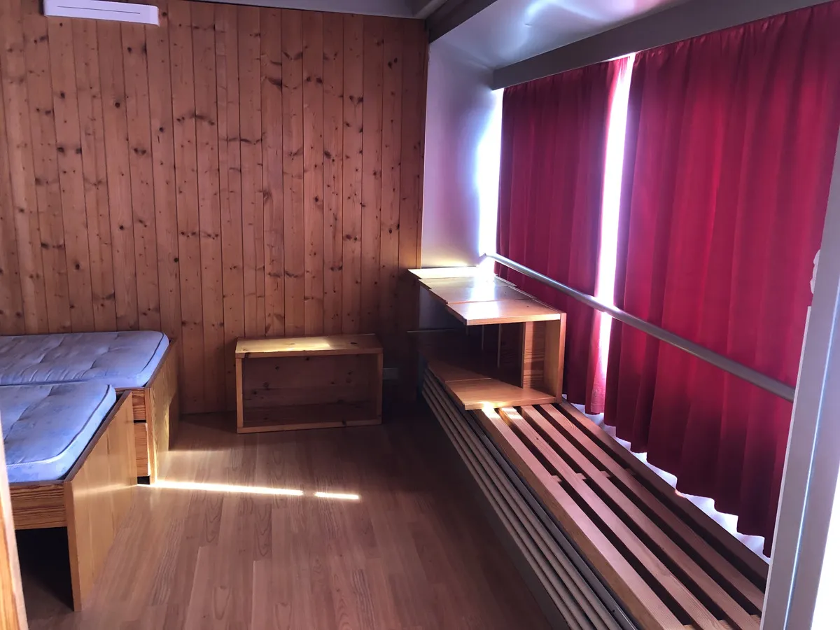 Camera con rivestimento in legno, letto singolo, tende rosse e mensole in legno