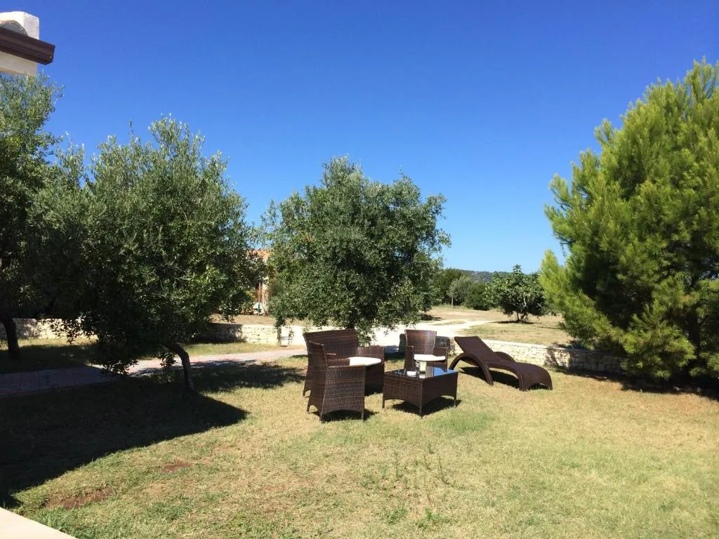Giardino con poltrone in rattan e lettino tra ulivi e pini