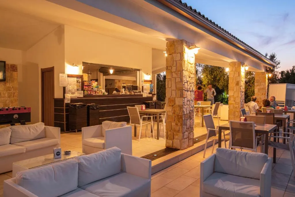 Bar lounge esterno illuminato al tramonto con divani bianchi e colonne in pietra