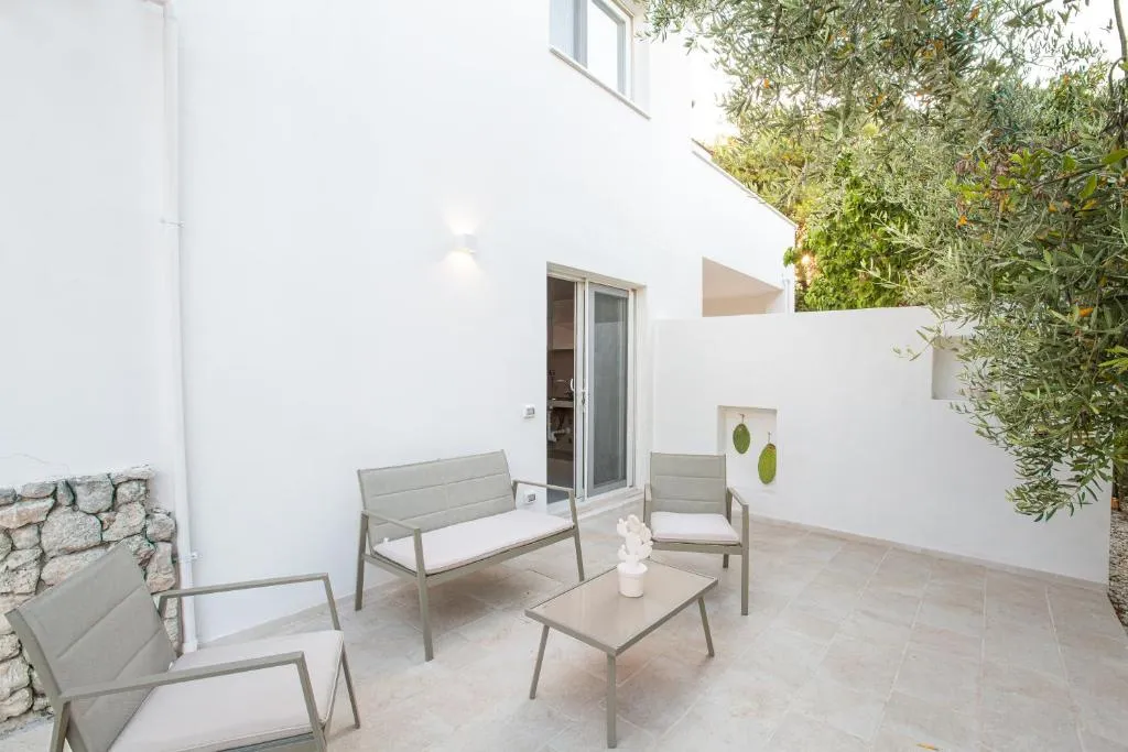 Patio esterno bianco con divani, poltrone e tavolino tra le piante