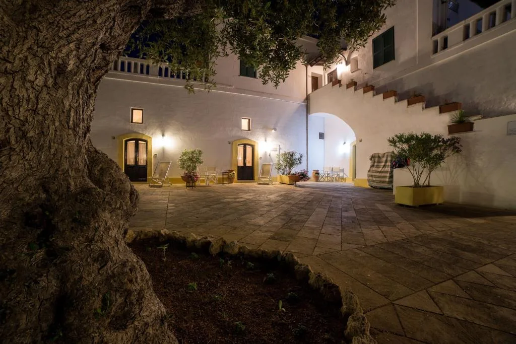 Cortile interno illuminato di notte con ulivo, archi e scala esterna