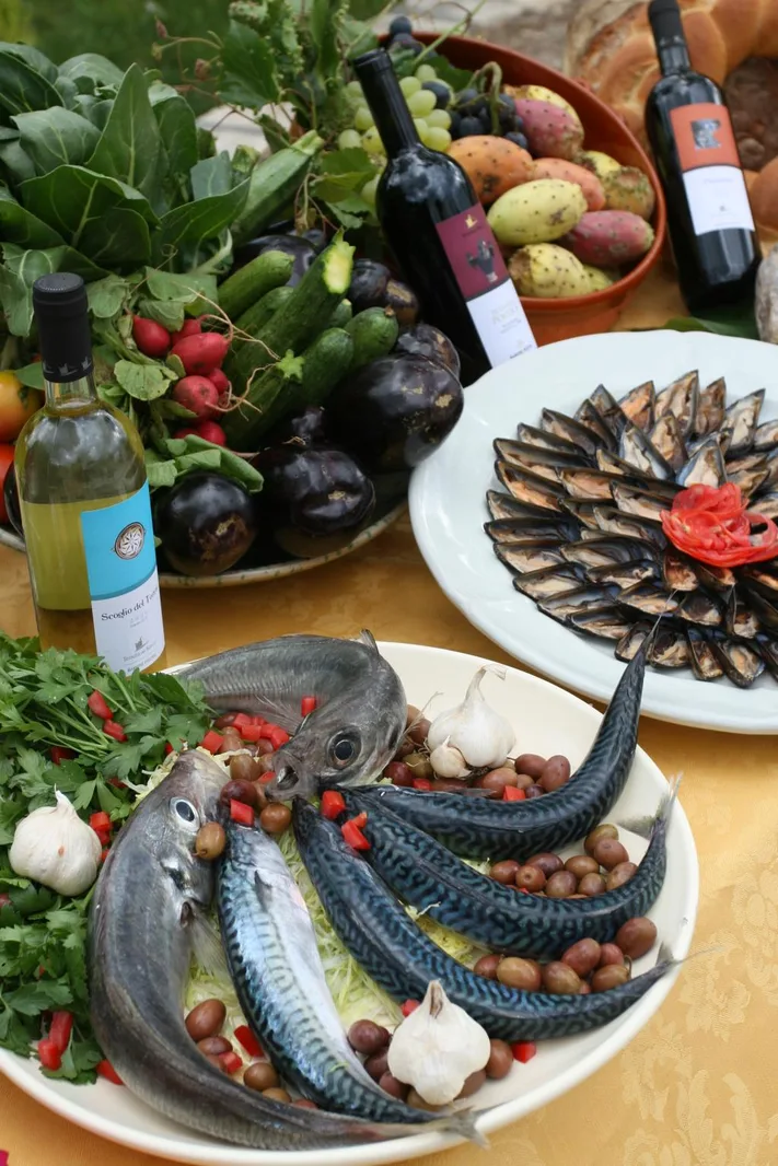 Piatti di pesce fresco, frutti di mare, verdure e bottiglie di vino locale