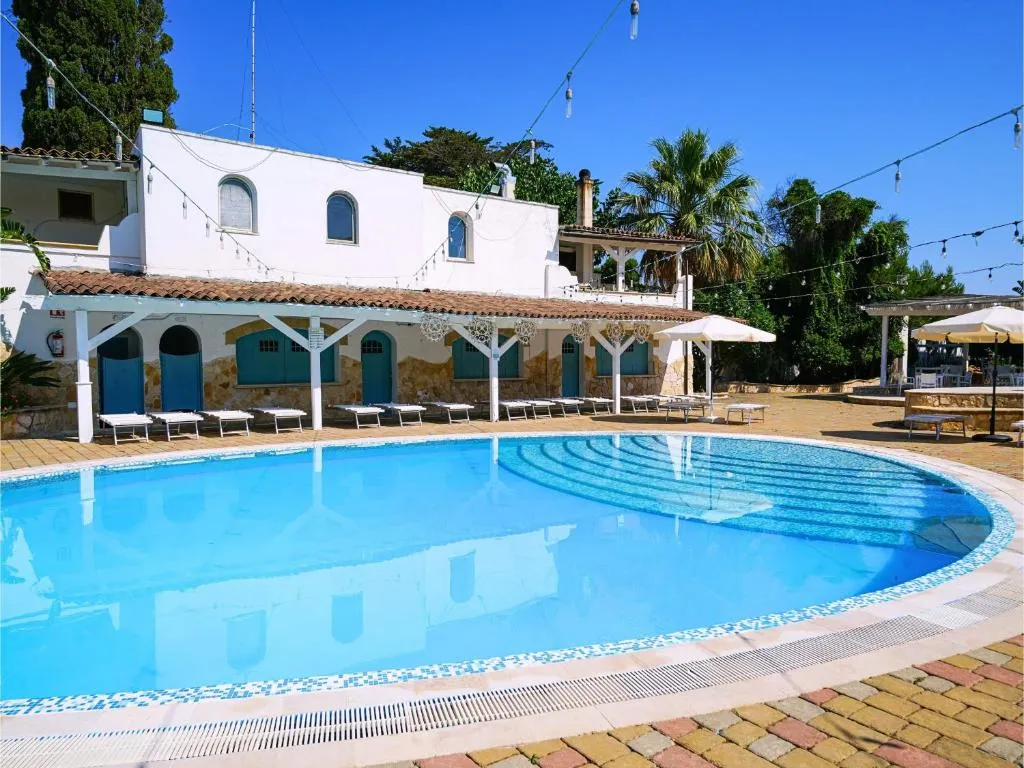Piscina azzurra con lettini ed edificio bianco in stile mediterraneo