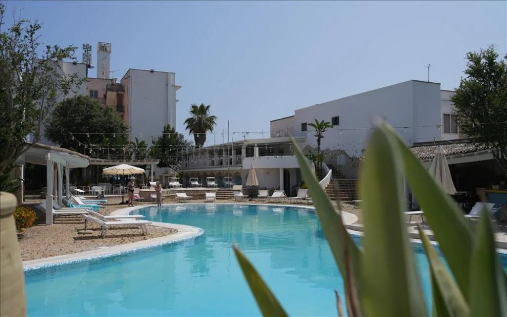 Piscina dell'hotel con lettini e ombrelloni circondata da edifici bianchi