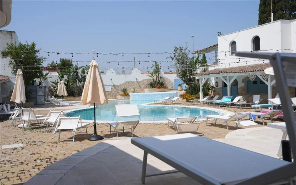 Area piscina con lettini, ombrelloni e edifici bianchi in stile mediterraneo
