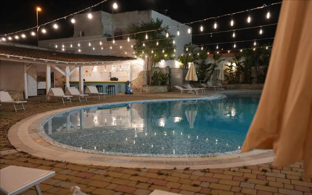 Piscina illuminata di sera con bar, lettini e luci decorative
