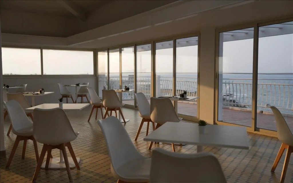 Sala colazione con tavoli, sedie bianche e vetrate con vista sul mare