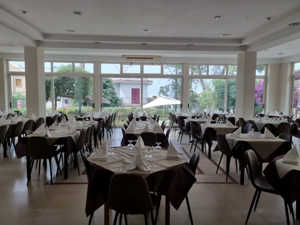 Sala ristorante con tavoli apparecchiati, sedie scure e ampie vetrate sul verde