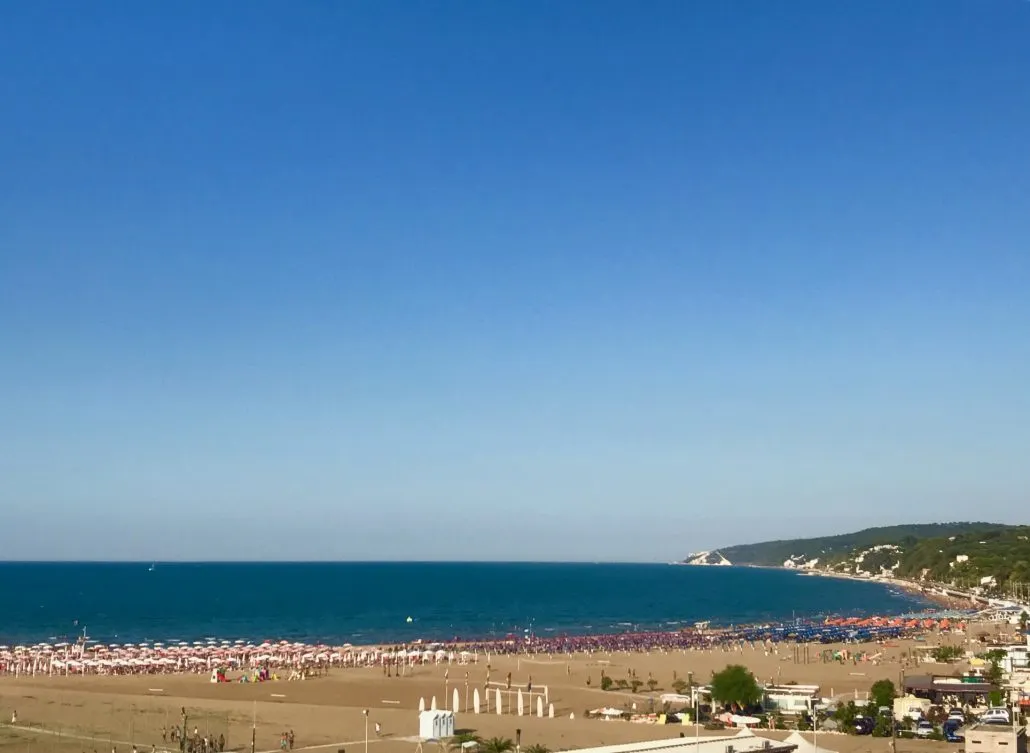 Panorama dall'alto della spiaggia con ombrelloni colorati, mare azzurro e promontorio